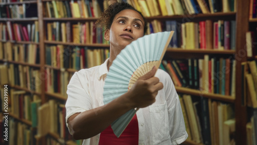 Foto Woman fanning face with pale blue handheld fan in a library building while tilting neck and closing eyes; heat relief