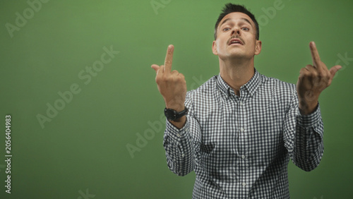 Photography Hispanic man flipping middle finger with both hands in green studio; defiance irreverence contempt attitude