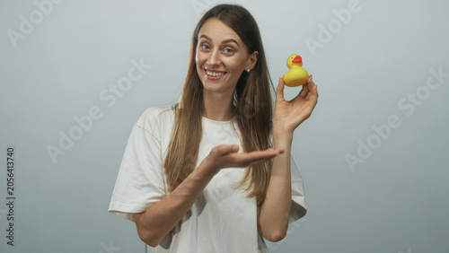 Foto Woman smiling and holding a yellow rubber duck in her right hand while presenting it with an open left palm in light gray studio; playful joy