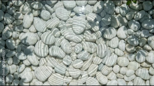 Droplet falling into clear water creating ripples over white pebbles. Zen stone background with liquid motion. Natural ripple pattern for relaxation and meditation.