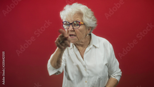 Obraz na płótnie Elderly woman in white shirt and glasses crosses arms and repeatedly points a finger while scolding in studio; stern reprimand