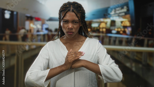 Fotografie Woman clutching chest with hands pressed over sternum in building, tense squinting expression and braided hair visible; pain concern urgency