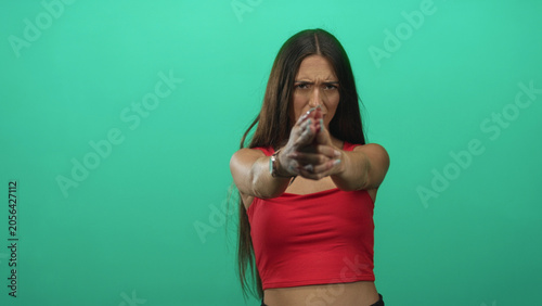 Φωτογραφία Young hispanic woman pointing fingers like a gun with hands extended in green studio; determination resolve focus strength