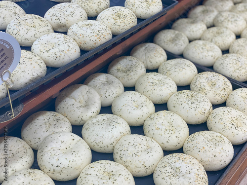 freshly baked herb bread rolls arranged on black trays in bakery display