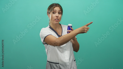 Foto Woman nurse young hispanic blonde pointing finger while holding a blue medicine bottle in studio; reassuring instruction