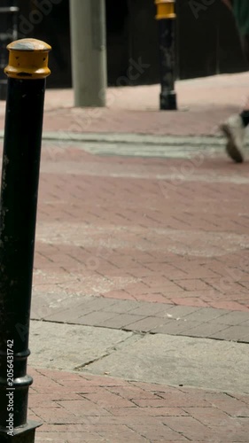 Vertical video: Framing bollard holding curb as people entering to cross, cyclist passing with bike
