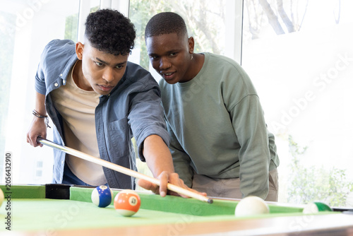 African American teenage males leaning over pool table aiming shot with cue stick over cue ball