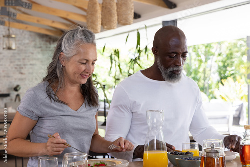 Couple with senior African American man and woman in gray T-shirt pouring orange juice at counter