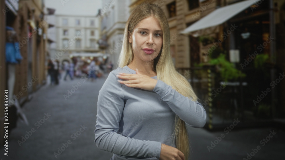 Fototapeta premium Woman touching long hair on a narrow street, adjusting her sweater and gazing sideways at storefronts; poised confidence.