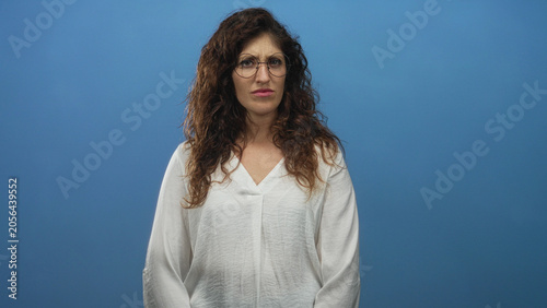 Fotografie Woman with beckoning hand gesture and tense facial expression in studio against blue backdrop; annoyance impatience