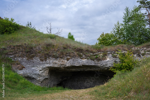 Konstfotografi a natural cave entrance carved into a grassy, rocky hillside under an overcast sky