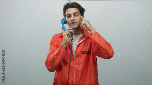 Canvastavla Man prisoner in orange jumpsuit holds blue handset to ear and points finger to cheek in studio; isolation reflection