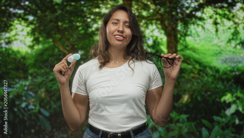 Bild auf Leinwand Woman holding eyeglasses and contact lens case in park, smiling with eyes closed; contentment and convenience