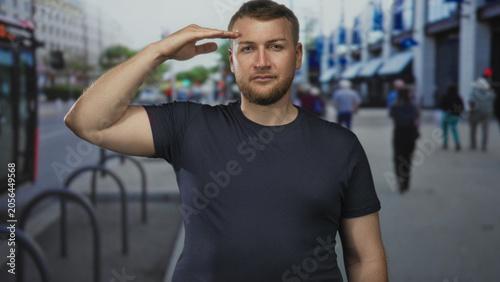 Obraz na plátne Man giving hand salute to forehead on a city street with bike racks and blurred pedestrians in the sidewalk; respect