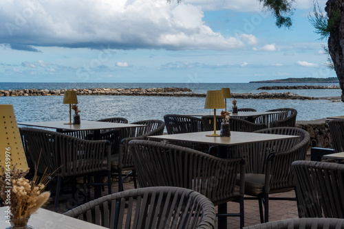 Cozy outdoor restaurant terrace shaded by a rustic bamboo roof, featuring wooden tables and a beautiful panoramic view of the blue sea and coast.