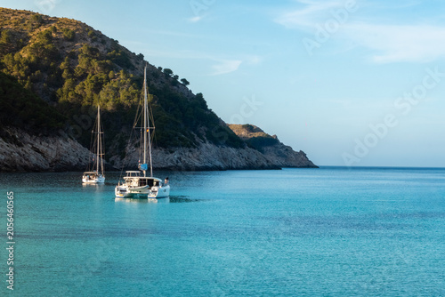Small boats anchored in a crystal-clear bay surrounded by rugged hills, capturing the calm beauty and peaceful atmosphere of a Mediterranean coastline.