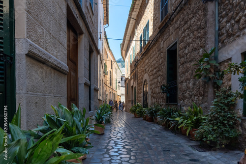 Charming narrow cobblestone street lined with historic stone buildings and lush greenery, capturing the authentic atmosphere of a Mediterranean old town.