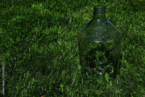 Obraz na plátně A large empty glass carboy or demijohn bottle standing outdoors on a green lawn in sunlight