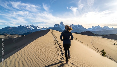 Active Woman Running Along Sandy Dune Ridge with Mountain Range Under Blue Sky