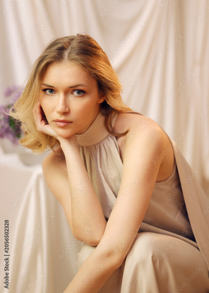 Naklejka premium Close-up beauty portraits of a blonde model in beige silk touching her face. Soft studio light, draped fabric, and lilacs. Ideal for skincare, cosmetics, jewelry, and fashion campaigns.
