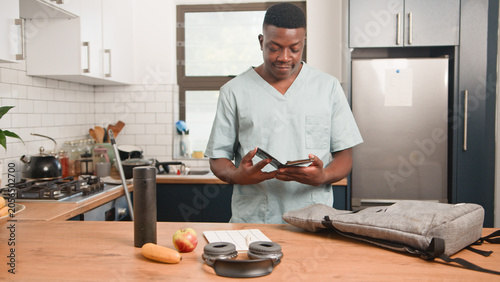 Healthcare Worker in Scrubs Checking Wallet at Kitchen Counter With Backpack and Water Bottle