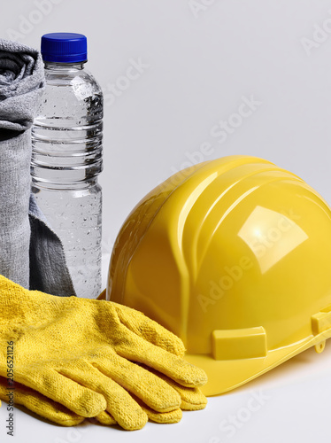 Workplace heat safety gear with hard hat gloves and water bottle on plain background