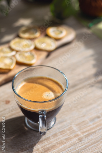 Glass cup of fresh espresso coffee on wooden table with blurred dried lemons on background