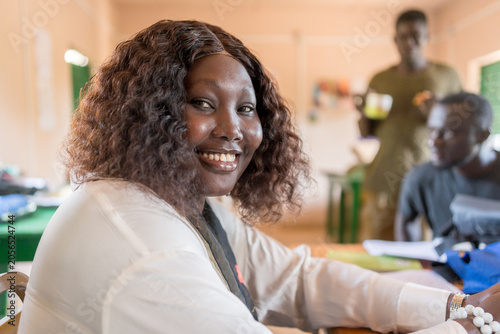 Portrait of smiling young african business woman sitting at desk in office writing and working in team on laptop,corporate jobs and economy in africa