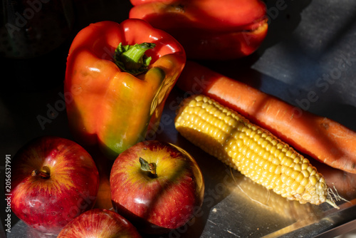 Photos Top view of fresh raw vegetables and red apples under harsh sunlight on a counter