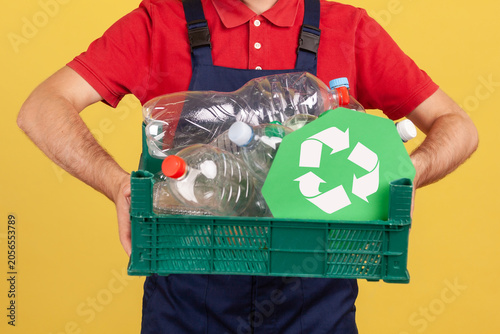 Anonymous worker holding box with plastic bottles for recycling to promote environmental protection or waste sorting isolated over yellow background with copy space