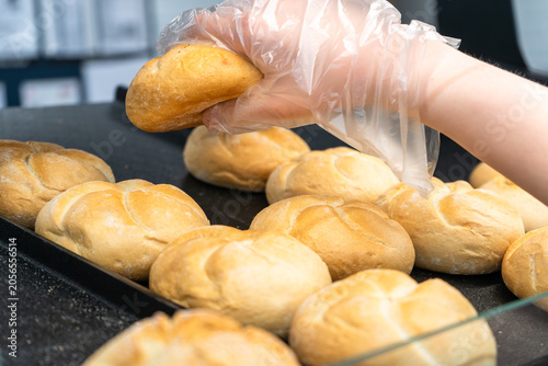 Fotografie Gloved hand lifting fresh bread roll from tray in self service bakery section