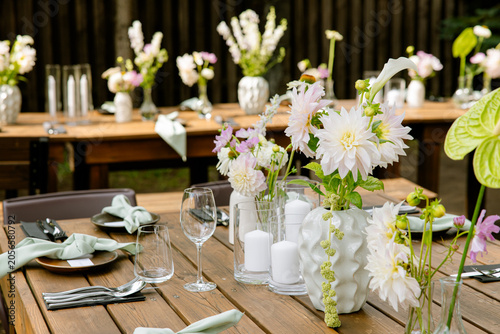 Wedding reception table detail with pink dahlia flowers wine glasses and sage green napkins on wooden surface at rustic outdoor barn venue