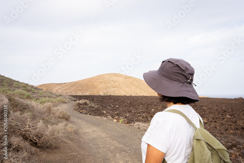 Obraz na płótnie Woman walking on dirt path through volcanic landscape, exploring arid nature, fi