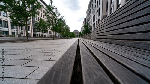 Low angle, close up of a wooden bench leading to a wide pedestrian walkway with modern buildings