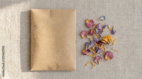 Top-down flat lay view of a blank craft paper seed packet next to dried flower petals on a linen fabric background