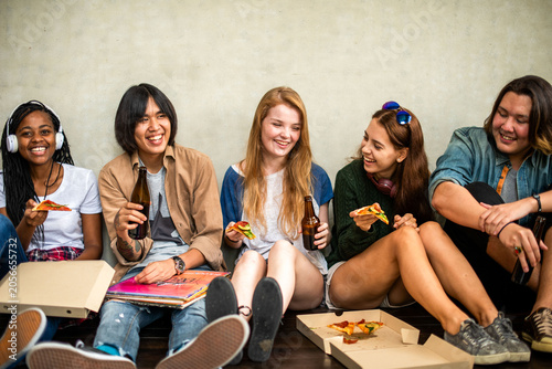 Obraz na płótnie Group of young adults sitting, eating pizza, and laughing together