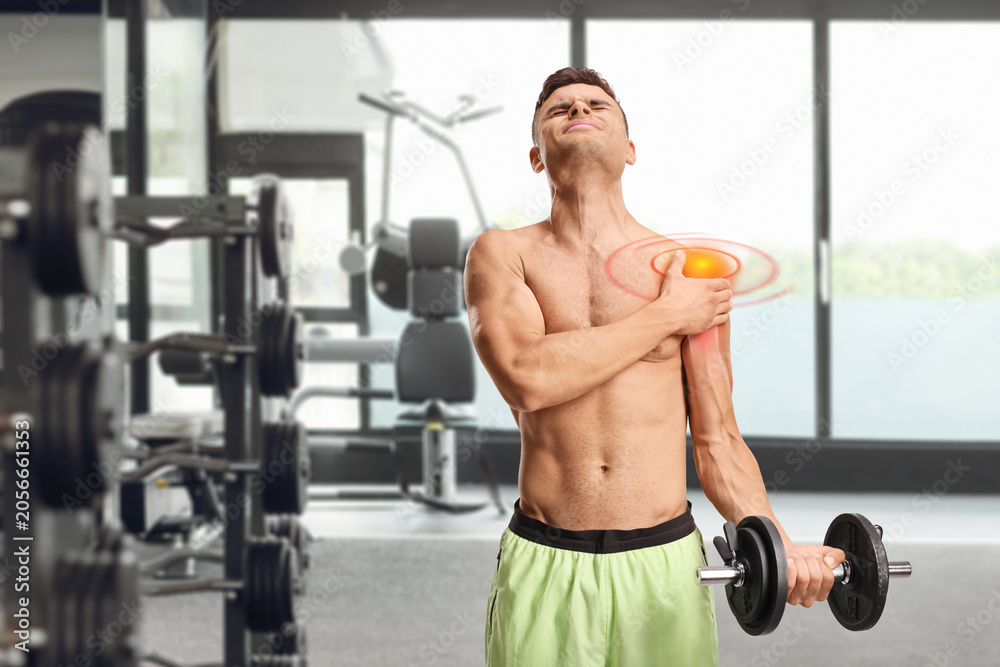 Fototapeta premium Young man suffering from shoulder pain and exercising with weights