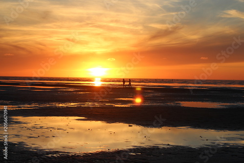 Canvastavla People walking on beach at sunset reflecting orange sky