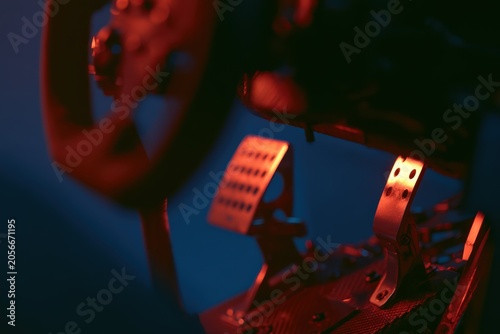 Close-up view of a premium sim racing steering wheel and pedals in a dark room with vibrant lighting, showcasing details and design features