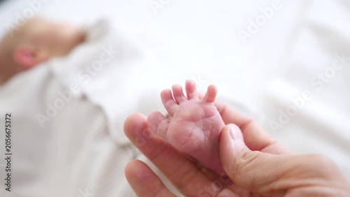 Gentle parent's hands carefully holding the tiny, delicate feet of a sleeping newborn baby, representing the concepts of family love, protection, and the beginning of a new life