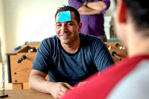 Konstfotografi Man with sticky note on forehead, smiling, playing a guessing game