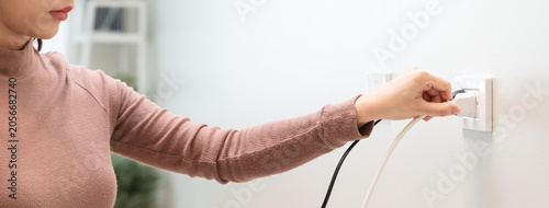 Εκτύπωση καμβά Close-up of woman hand plugging or unplugging an electrical cord into a wall socket, energy saving concept