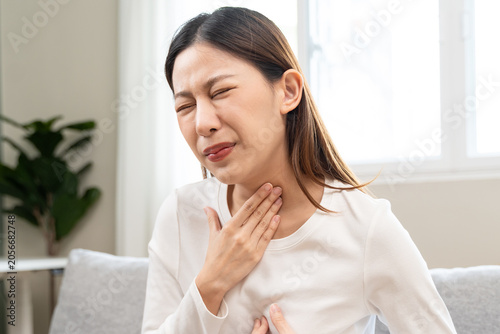 Fotografie Unhappy female feeling painful with heartburn or acid reflux symptom, touching her throat and chest on sofa