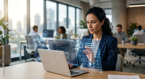 A woman works on her laptop in a modern office environment with colleagues.