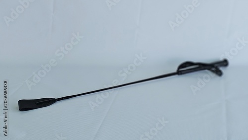 Foto Black riding crop rests on a plain white surface