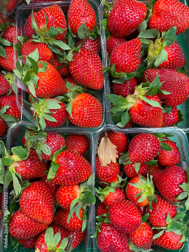 Fresh ripe strawberries displayed in transparent containers at a local market. Vibrant red berries with green leaves create a healthy food background, perfect for agriculture, nutrition and summer