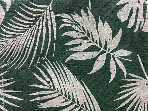 Tropical leaf pattern printed on woven natural fiber texture. White botanical silhouettes on dark green background create an elegant exotic design for decor, textiles and backgrounds.