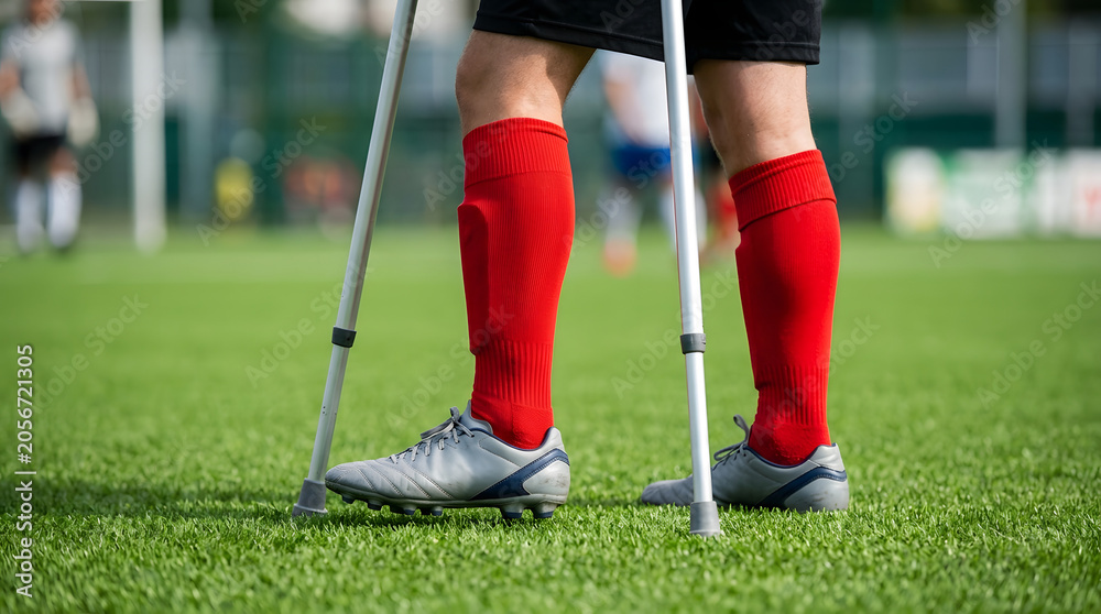 Obraz premium Injured athlete on crutches in red socks on grass soccer field recovery training. Generative AI image