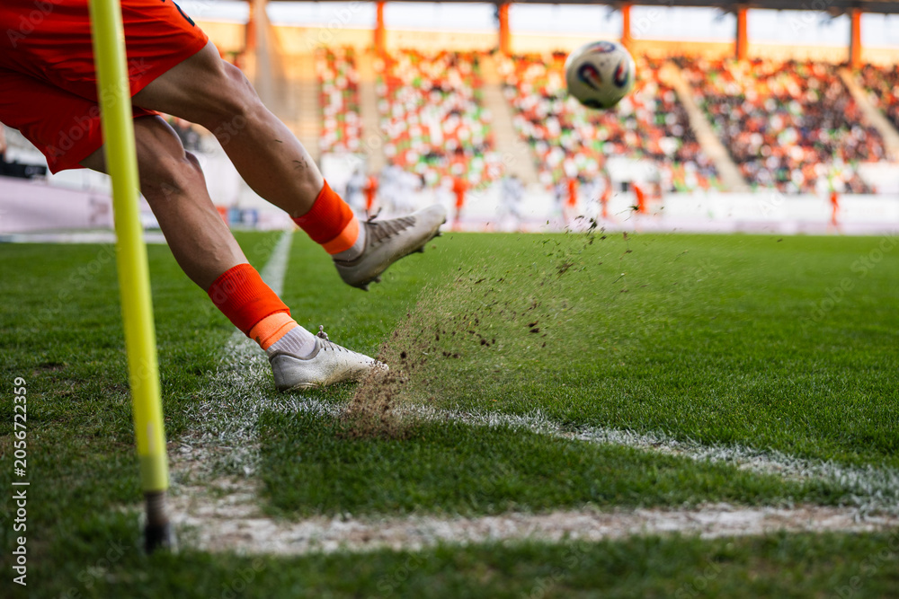 Naklejka premium A close-up of a soccer player's legs kicking a ball during a corner kick with turf and dust flying up at a stadium.