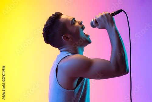 Energetic male singer performing with microphone, expressive musician shouting in neon lighting, vibrant pop star portrait on colorful gradient background